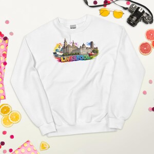Könnte beinhalten: Ein weißes Sweatshirt mit Rundhalsausschnitt und einer farbenfrohen Aquarellgrafik der Skyline von Liverpool. Das Design zeigt detaillierte architektonische Gebäude und das Wort LIVERPOOL in fetten, bunten Buchstaben auf der Brust.