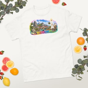 Könnte beinhalten: Ein weißes T-Shirt mit einem farbenfrohen Grafikdruck von Yogyakarta, Indonesien. Die Abbildung zeigt einen Tempel, ein hohes Denkmal, Palmen und eine Berglandschaft mit dem Schriftzug YOGYAKARTA in fetten, bunten Buchstaben.