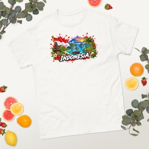 Könnte beinhalten: Ein weißes T-Shirt mit einem farbenfrohen Grafikdruck der indonesischen Flagge, einem traditionellen Tempel, einer tropischen Landschaft mit Palmen und einem Gebirge. Das Wort INDONESIA ist in fetten schwarzen Buchstaben aufgedruckt.