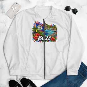 May include: A white bomber jacket featuring a central graphic print of the Belize flag, a toucan, tropical flowers, and a coastal landscape with the text BELIZE. The jacket has a full-length black zipper, long sleeves, and ribbed collar and cuffs.