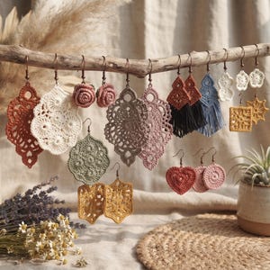 May include: A collection of various crochet earrings hanging from a wooden branch. The earrings feature diverse shapes including intricate lace-like teardrops, small roses, hearts, circles, and squares in colors like rust, cream, sage, pink, and blue.