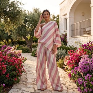 May include: A two-piece set consisting of a one-shoulder top with wide sleeves and matching wide-leg trousers, both featuring a diagonal striped pattern in soft pink and cream colors, creating a coordinated outfit with a relaxed silhouette.