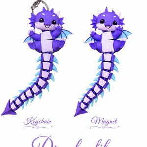 Könnte beinhalten: Zwei lila Drachenfiguren mit helllila Bäuchen, blauen Flügeln und segmentierten Schwänzen. Eine Figur ist an einem silbernen Metallschlüsselanhänger befestigt, die andere ist ein Magnet. Der Text "Keychain", "Magnet" und "Drache lila" ist zu sehen.