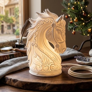 May include: A white, illuminated horse head lamp featuring intricate, carved-style scrollwork patterns across its surface. The lamp emits a warm, soft glow from within and includes a coiled white power cord extending from its base.