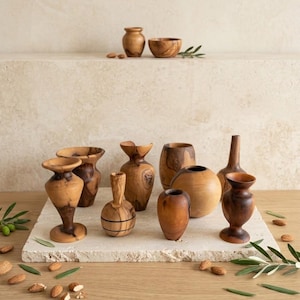 Peut inclure: Une collection de petits vases et bols en bois d'olivier tournés à la main, présentant des motifs de grain naturels et des tons brun chaud. L'ensemble comprend diverses formes, telles que des vases sur pied, des récipients sphériques et un petit bol.