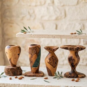 May include: Four handcrafted wooden vessels made from olive wood with natural grain patterns and bark edges. One vessel features a vertical green resin inlay with horizontal stripes. The items are displayed on a stone surface with scattered almonds.