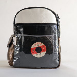 Può includere: Zaino in vinile nero, bianco e marrone con una tasca trasparente in vinile che presenta un disco in vinile vintage con il testo "COLGEMS THE MIRACLES HIT THE  " e "COME  ON  AND  DO  THE  STOMP".