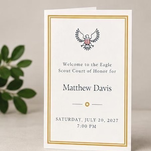 May include: A white folded card with a gold double-line border featuring a black and red eagle emblem. The text reads: Welcome to the Eagle Scout Court of Honor for Matthew Davis, Saturday, July 20, 2027, 7:00 PM, with a small gold star.