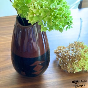 May include: A teardrop-shaped ceramic vase with a glossy finish, featuring a two-tone design of dark brown on the upper portion and black on the lower section, accented with a geometric diamond pattern. Bright green hydrangea flowers are inside.