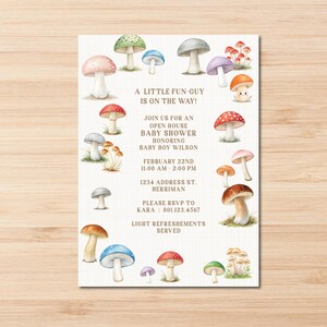 Könnte beinhalten: Eine Babyparty-Einladung mit einem Pilz-Motiv. Die Einladung zeigt eine Aquarell-Illustration von Pilzen in verschiedenen Farben und Größen. Der Text auf der Einladung lautet "A Little Fun-Guy is on the Way!" und enthält Details zur Veranstaltung, wie Datum, Uhrzeit und Ort.