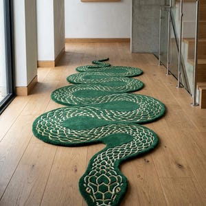Puede incluir: Una alfombra larga con forma de serpiente en color verde intenso con un patrón de escamas de color crema. La alfombra presenta una forma sinuosa y serpentina que se extiende por el suelo, mostrando una cabeza detallada y un cuerpo largo y curvado.