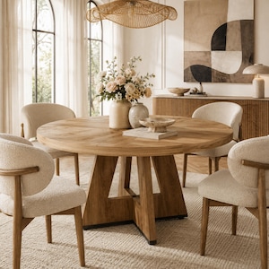 May include: A round wooden dining table with a chevron pattern top and a sturdy pedestal base, surrounded by four cream-colored upholstered chairs with curved wooden frames, featuring a floral centerpiece in a ceramic vase.