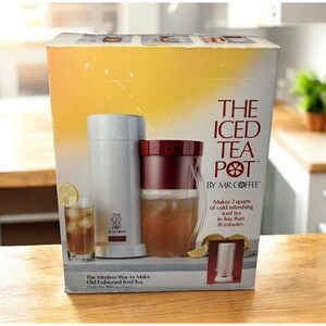 Può includere: Una scatola di cartone rettangolare per The Iced Tea Pot di Mr. Coffee. La scatola presenta uno sfondo sfumato bianco e giallo con immagini di una macchina per il tè bianca e una caraffa bordeaux piena di tè freddo. Il testo include The Iced Tea Pot.