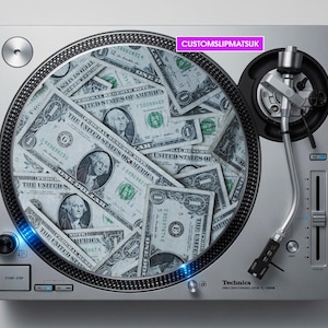 May include: A silver Technics SL-1200MK turntable featuring a custom slipmat printed with a collage of United States one-dollar bills. The turntable includes a tonearm, a start-stop button, and a pink rectangular label with the text CUSTOMSLIPMATSUK.