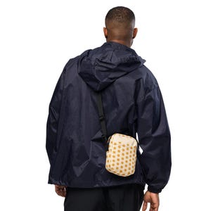 May include: A navy blue hooded windbreaker jacket worn with a small, rectangular crossbody bag. The bag features a cream-colored base with a repeating pattern of mustard yellow polka dots and includes a black adjustable shoulder strap.