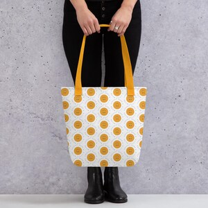 Könnte beinhalten: Eine weiße Tragetasche mit senfgelben Trägern und einem wiederkehrenden Muster aus senfgelben Smileys. Jeder Smiley ist von dem Text "little things matter" in einer kreisförmigen blauen Schrift umgeben. Die Tasche hat eine flache Form.