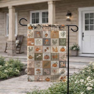 May include: A rectangular garden flag featuring a grid pattern of squares with illustrations of pumpkins, mushrooms, acorns, flowers, and foliage in muted earth tones of orange, brown, green, and beige, suspended on a black metal stand.