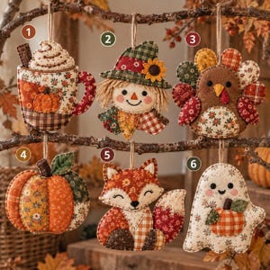 May include: Six fabric ornaments featuring autumn themes: a mug with whipped cream, a scarecrow, a turkey, a pumpkin, a fox, and a ghost holding a pumpkin. Each piece is crafted from various patterned textiles in orange, brown, and green tones.