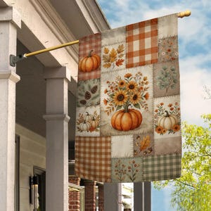 May include: A rectangular garden flag featuring a patchwork design with autumn themes. The pattern includes orange pumpkins, sunflowers, brown and white gingham checks, pinecones, fall leaves, and sprigs of berries on a cream-colored background.