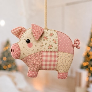 May include: A hanging fabric pig ornament featuring a patchwork design of pink and cream textiles. The pig is constructed from various patterns including floral prints, gingham checks, and polka dots, with a small curled tail and a black bead eye.