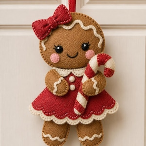 May include: A felt gingerbread ornament featuring a brown cookie figure wearing a red dress with a scalloped white trim, a red bow on its head, and pink cheeks. The figure holds a red and white striped candy cane and hangs from a red ribbon.