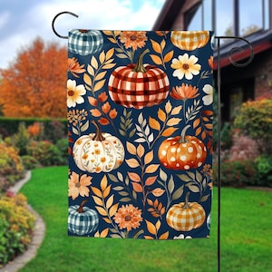 May include: A rectangular garden flag featuring a dark navy blue background with a repeating pattern of various pumpkins and autumn leaves. The pumpkins include red plaid, white floral, orange polka dot, and blue plaid designs among orange flowers.