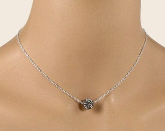 Puede incluir: Un collar de cadena en tono plateado con un colgante esférico único incrustado con pequeños cristales de color gris oscuro. La delicada cadena de metal se conecta a la cuenta central, creando un diseño sencillo sobre la clavícula.