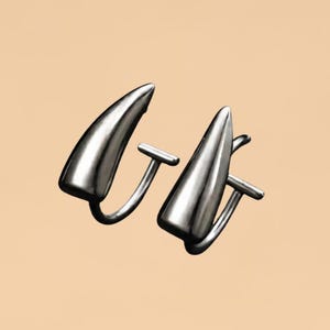 May include: A pair of silver-toned earrings featuring a smooth, curved, horn-like or fang-shaped design. Each earring has a polished metallic finish and a simple post-back closure mechanism, presenting a sleek and uniform appearance throughout.
