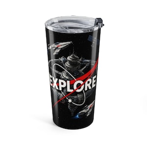May include: A black stainless steel tumbler with a clear plastic lid featuring a space-themed graphic. The design includes a large space station, two spacecraft, and the word EXPLORE in white capital letters with a red swoosh graphic.