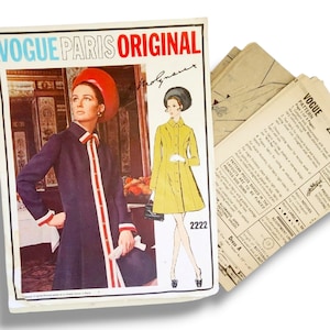 May include: A Vogue Paris Original sewing pattern envelope 2222 featuring a photograph of a dark blue coat with red and white trim, alongside a yellow coat illustration. The set includes printed paper pattern instruction sheets with text.