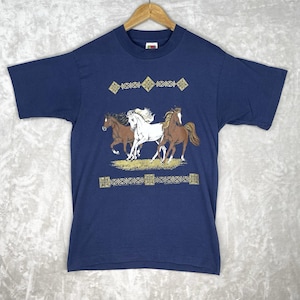 May include: A navy blue short-sleeve t-shirt featuring a graphic of three horses running across a field. The design includes a white horse flanked by two brown horses, framed by decorative gold-colored geometric borders above and below.