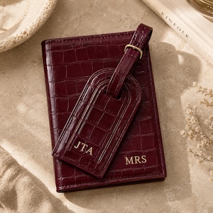 May include: A deep burgundy passport holder and matching luggage tag with a crocodile-embossed texture. The passport holder features the gold-embossed text MRS, while the luggage tag displays the gold-embossed initials JTA on the front.