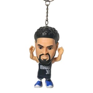 May include: A keyring featuring a small figurine of a basketball player with dark hair and a beard. The figure wears a black jersey with the text MAVS and the number 31 printed in white on the front, paired with blue and white athletic shoes.