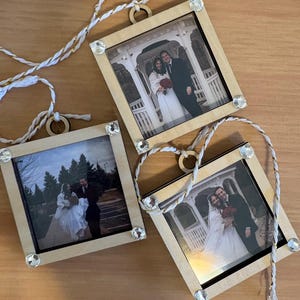 May include: Three square wooden photo ornaments featuring wedding pictures. Each light-colored wood frame is accented with four clear rhinestones at the corners and includes a white and gold twisted hanging cord attached to a circular loop.