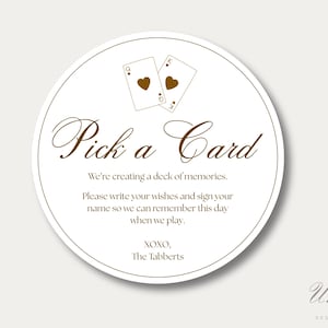 K&ouml;nnte beinhalten: Ein kreisf&ouml;rmiges Schild mit wei&szlig;em Hintergrund und braunem Rand. Es zeigt zwei Spielkarten mit Herzen, den Text "Pick a Card", "We're creating a deck of memories. Please write your wishes and sign your name so we can remember this day when we play. XOXO, The Tabberts".