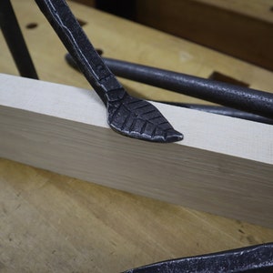 May include: A close-up of a black metal leaf-shaped tool resting on a light wood surface. The tool is part of a set of tools used for woodworking.