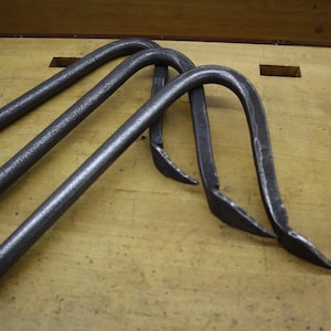 Pu&ograve; includere: Tre ganci in metallo con forma curva e estremit&agrave; appuntite. I ganci sono in metallo grigio scuro e sono appoggiati su una superficie di legno.