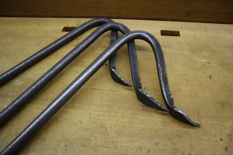 Pu&ograve; includere: Tre ganci in metallo con forma curva e estremit&agrave; appuntite. I ganci sono in metallo grigio scuro e sono appoggiati su una superficie di legno.