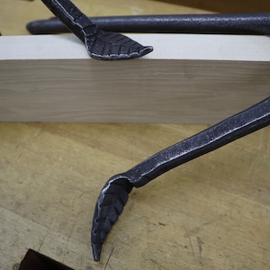 Pu&ograve; includere: Due morsetti in metallo nero con estremit&agrave; a forma di foglia sono fissati su un pezzo di legno.