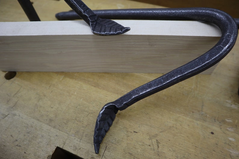 Pu&ograve; includere: Due morsetti in metallo nero con estremit&agrave; a forma di foglia sono fissati su un pezzo di legno.