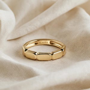 Könnte beinhalten: Ein goldener Ring, der aus einer Reihe verbundener, glatter, rechteckiger Segmente besteht, die das Band bilden. Die Innenseite des Rings ist mit dem Namen Emma in einer klaren, dunklen Serifenschrift graviert und hat ein poliertes Finish.