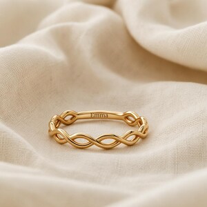 May include: A gold-toned ring featuring a continuous twisted rope or infinity-style band design. The outer surface of the ring is engraved with the name Emma in a clear, dark, sans-serif font, centred along the top section of the metal band.