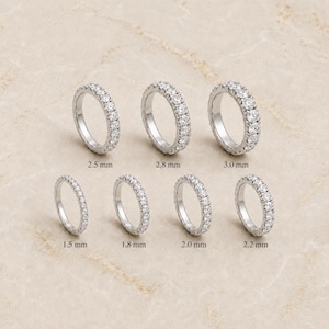 May include: Seven silver-toned eternity rings set with clear round stones, arranged in two rows. The rings are labeled with widths of 1.5 mm, 1.8 mm, 2.0 mm, 2.2 mm, 2.5 mm, 2.8 mm, and 3.0 mm, indicating the varying thickness of each individual band.