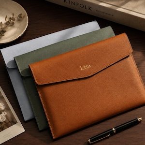 May include: Three rectangular document sleeves with envelope-style flaps, stacked in tan, olive green, and light blue. The tan sleeve features the name Lisa embossed in gold lettering on the front flap. Each sleeve has a textured finish.