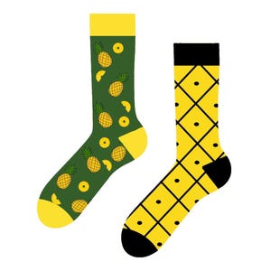 May include: A pair of crew socks featuring two distinct designs. The left sock is dark green with a yellow pineapple and slice pattern, yellow cuff, heel, and toe. The right sock is yellow with a black diamond grid pattern and black cuff and toe.
