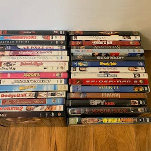 May include: A collection of DVDs stacked on a wooden surface. Titles include "Big Momma's House," "Batman Begins," "Air Force One," "13 Going on 30," "My Big Fat Greek Wedding," "School Rock," "Johnny English," and "Dodgeball."