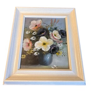 Pu&ograve; includere: Dipinto di natura morta floreale incorniciato. L'opera presenta un bouquet di fiori colorati in un vaso blu. I fiori includono fiori rosa, bianchi e viola. Il dipinto &egrave; ambientato in una cornice di legno bianca.