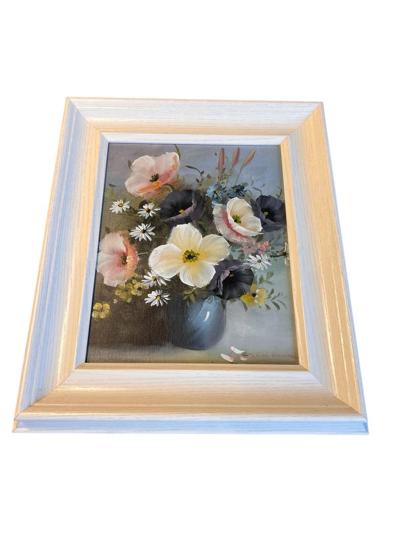 Pu&ograve; includere: Dipinto di natura morta floreale incorniciato. L'opera presenta un bouquet di fiori colorati in un vaso blu. I fiori includono fiori rosa, bianchi e viola. Il dipinto &egrave; ambientato in una cornice di legno bianca.