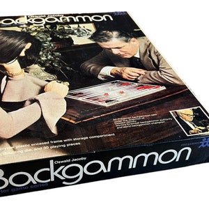 May include: A rectangular cardboard box for an Oswald Jacoby Backgammon parlor game series. The box features a photograph of two people playing backgammon on a wooden table, with text detailing the clear plastic frame and game components.