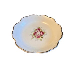 Pu&ograve; includere: Un piccolo piatto bianco con bordo smerlato e rifinitura dorata. Il centro del piatto presenta un motivo floreale con rose rosa e rosse e foglie verdi. Il piatto &egrave; probabilmente in porcellana o ceramica.